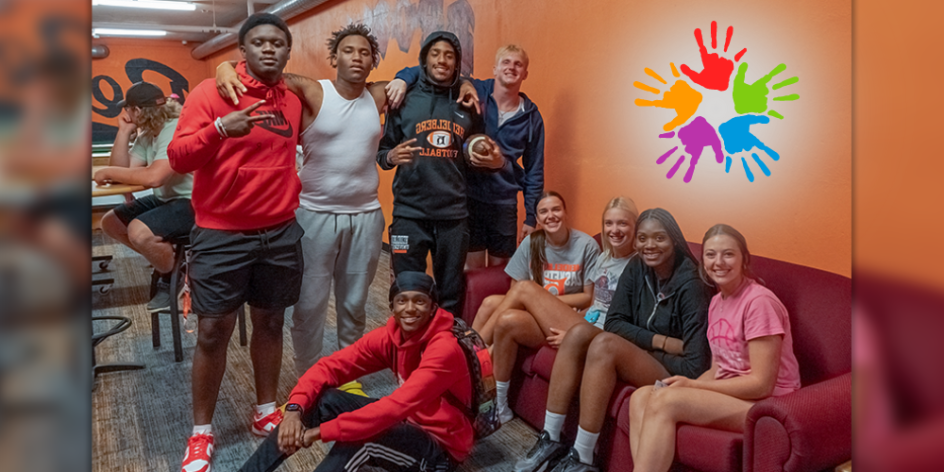 A group of several diverse students hanging out in the Brown basement lounge. The walls are orange and an image of 5 multicolor hands is superimposed.